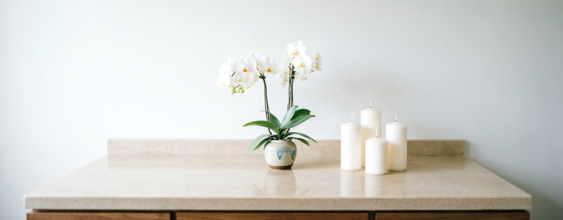 White silk orchid arrangement and pillar candles on a clean bathroom vanity counter, creating a spa-like atmosphere without sunlight